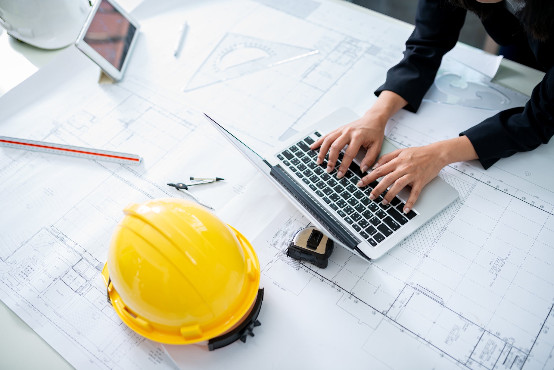 Hausbau Planung mit Bau-Elze: Laptop, Baupläne und Schutzhelm für professionelle Bauberatung und Baufinanzierung