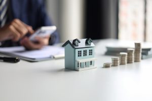 Modellhaus neben gestapelten Münzen als Symbol für die Kalkulation von Hausbaukosten und Budgetplanung